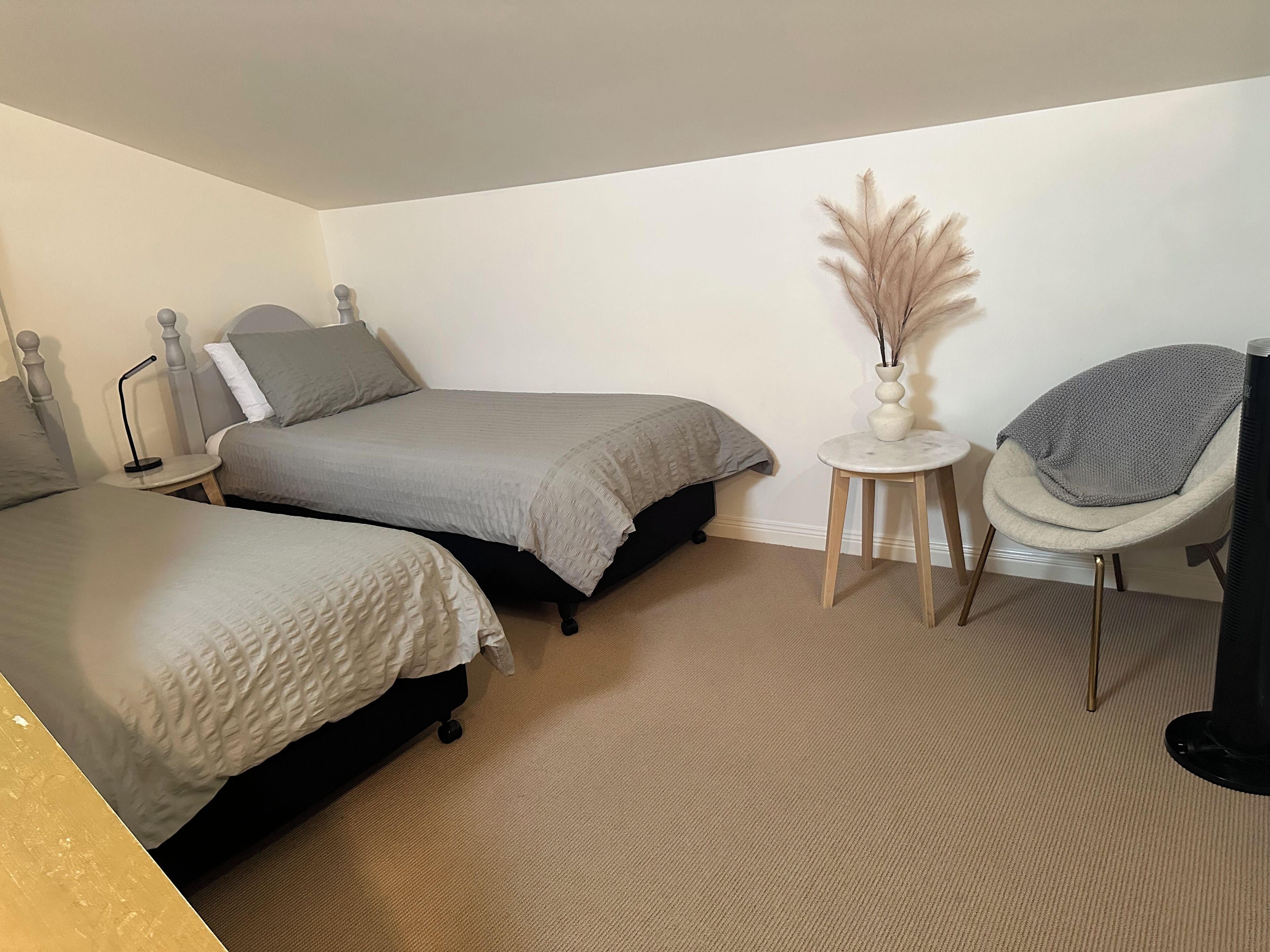 Een slaapkamer met twee bedden, een tafeltje met een vaas, een stoel en een televisie.