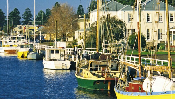A marina with several boats docked, a white building with a green roof, and a clear blue sky. - Austral Place 88 over Merri River (Dennington)