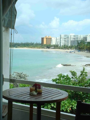Ein Balkon mit Tisch, mit Blick auf einen Strand und Gebäude im Hintergrund.