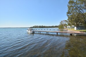 A calm lake with a dock extending into the water, surrounded by trees and a clear sky. - Edgewater Studio at Morisset Memories (Morisset Park)