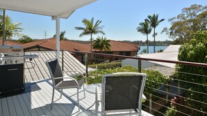 Une terrasse dotée de mobilier d’extérieur, d’un barbecue et offrant une vue sur une étendue d’eau bordée de palmiers.