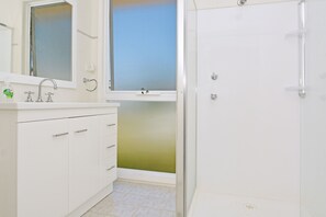 A bathroom with a white sink, mirror, and cabinet, a shower with a glass door, and a window above the sink.