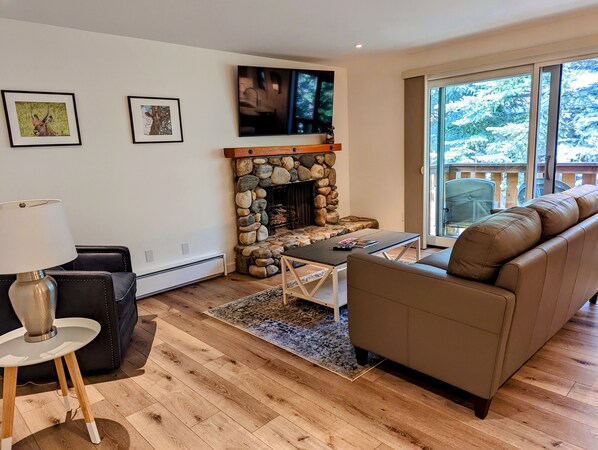 A living room with a stone fireplace, a sofa, a coffee table, and a TV mounted on the wall.