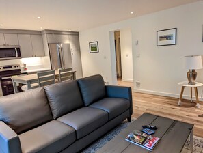 A modern living room with a grey sofa, a coffee table with magazines, a remote control, and a lamp.