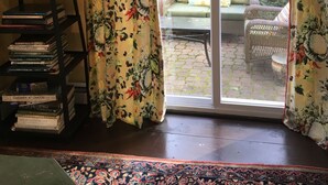 A room with a bookshelf, a patterned curtain, and a sliding glass door leading to an outdoor seating area. - Charming, river front compound  (Bantam)