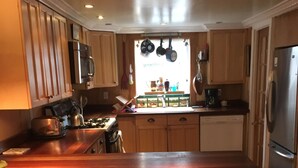 A modern kitchen with wooden cabinets, a stainless steel refrigerator, and a large island with bar stools. - Charming, river front compound  (Bantam)