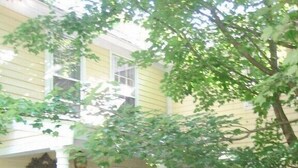 A yellow building with a porch, a wooden bench, and a white chair. - Charming, river front compound  (Bantam)