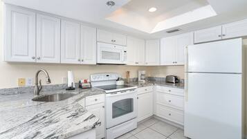 A modern kitchen with white cabinets, a granite countertop, a built-in microwave, a stove, and a refrigerator.