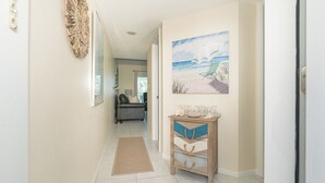 Un couloir avec un mur de couleur beige, une console en bois dotée de tiroirs, un tableau représentant une scène de plage et une porte donnant sur une autre pièce.