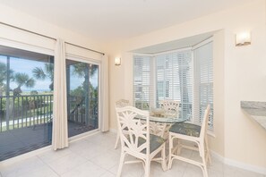 Spiseområde med et glasbord og hvide stole, en balkon med udsigt til palmer, og en skydedør i glas.