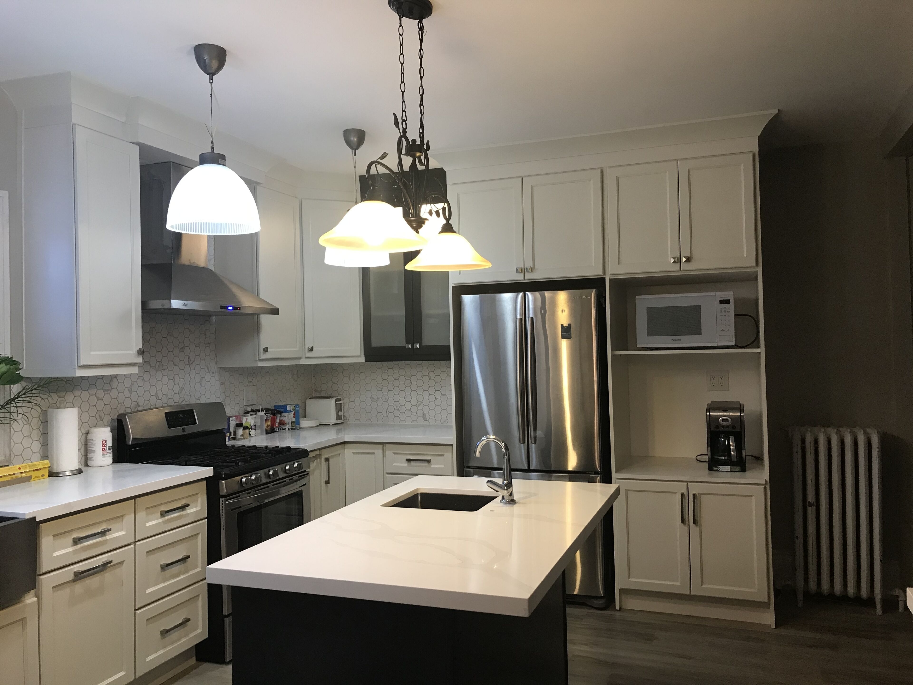 A modern kitchen with white cabinets, stainless steel appliances, a central island, and pendant lighting.