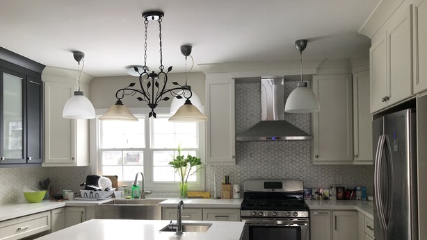 Una cocina moderna con armarios blancos, una isla central, electrodomésticos de acero inoxidable, iluminación colgante y vistas al exterior.