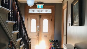 Una escalera de madera con barandilla blanca, un candelabro y un par de puertas dobles con un vitral.