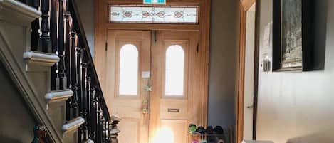 Una escalera de madera con barandilla blanca, un candelabro y un par de puertas dobles con un vitral.