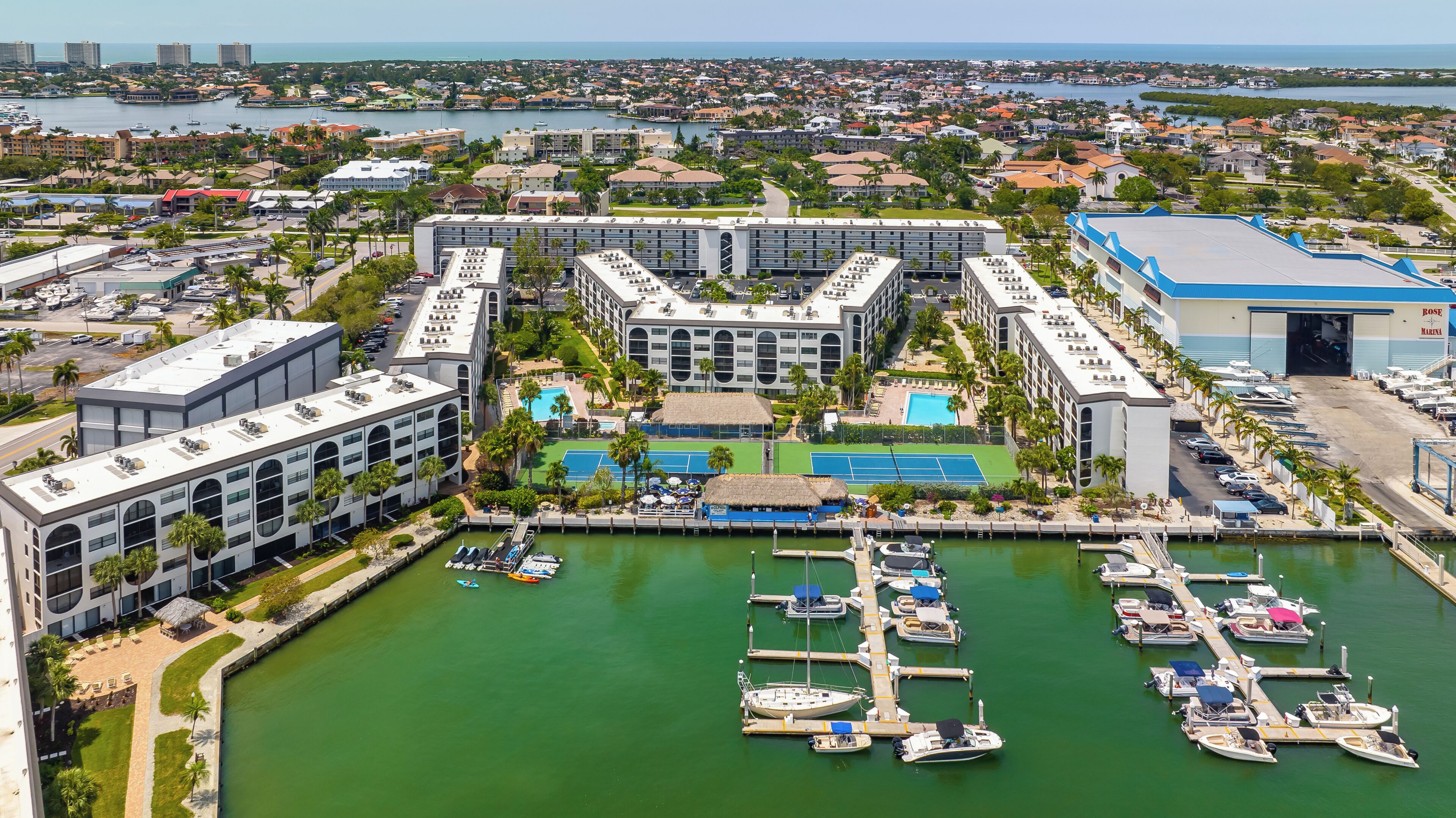 Un port de plaisance avec des bateaux amarrés, un espace piscine et un grand bâtiment à plusieurs étages.