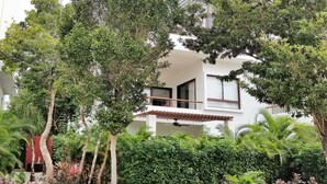 A modern building with a covered outdoor seating area, surrounded by lush greenery and trees.