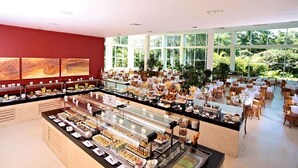 A buffet with various food stations, a seating area with tables and chairs, and large windows offering a view of greenery.