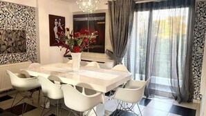 A dining area with a white table, six white chairs, a vase with red flowers, and a chandelier. - Greek hospitality with Free Double Parking and 1 Gbps WiFi / 9 persons (Κamatero)