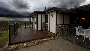 A covered outdoor deck with a stone wall, a wooden floor, and a chair.