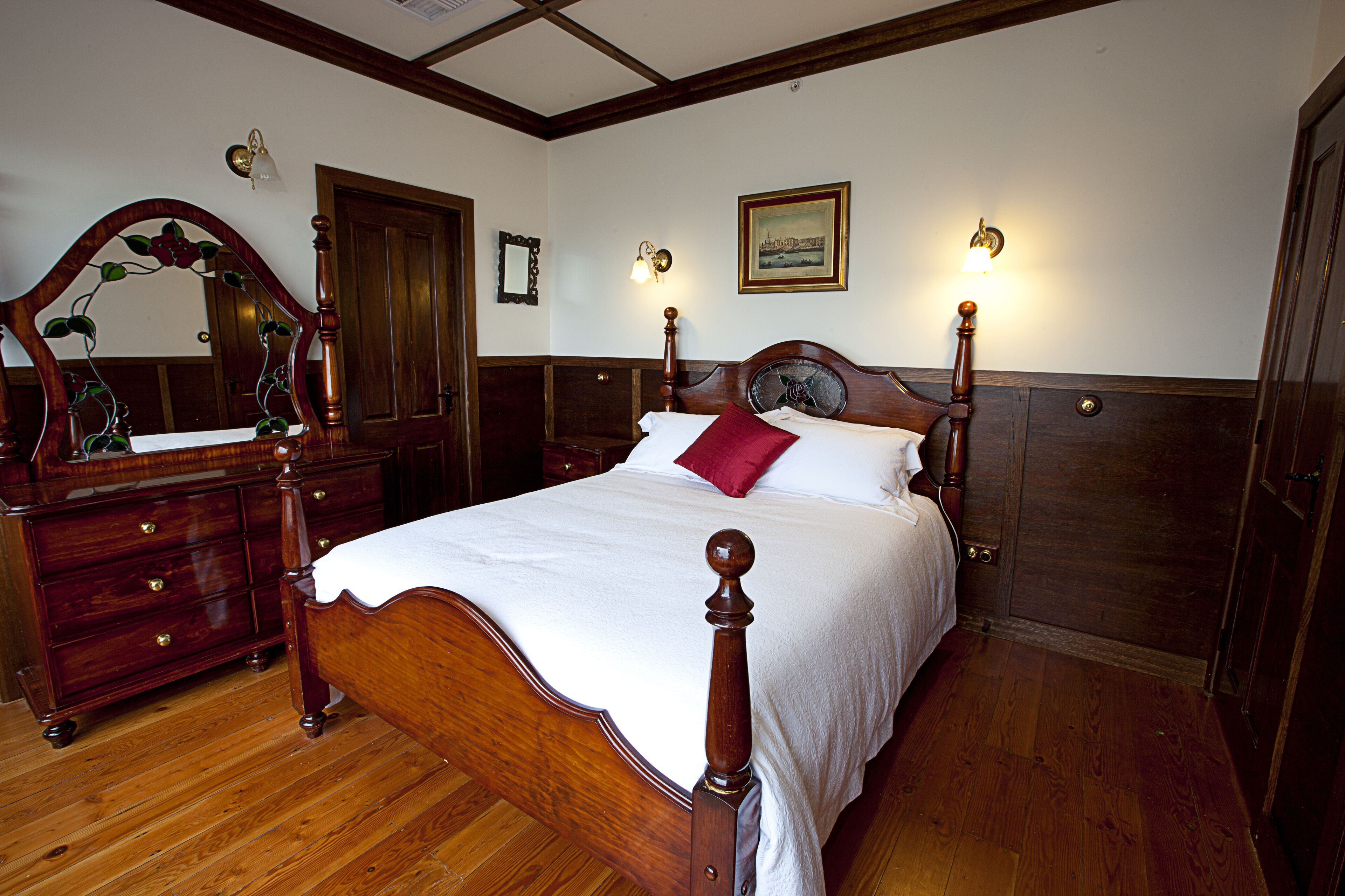 A traditional bedroom with a wooden bed, a dresser, and a mirror.