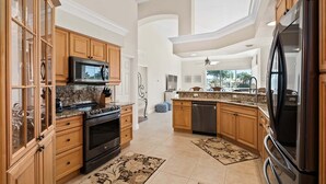 A spacious kitchen with wooden cabinets, a stainless steel refrigerator, and a granite countertop. - Waterfront 4BR Marco Island home with heated pool and space for 8. (Marco Island)