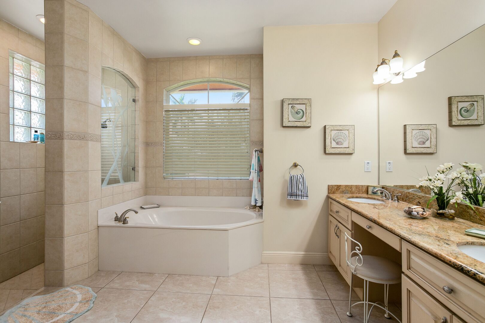 A bathroom with a large bathtub, a vanity with a sink, a mirror, and framed artwork on the wall.