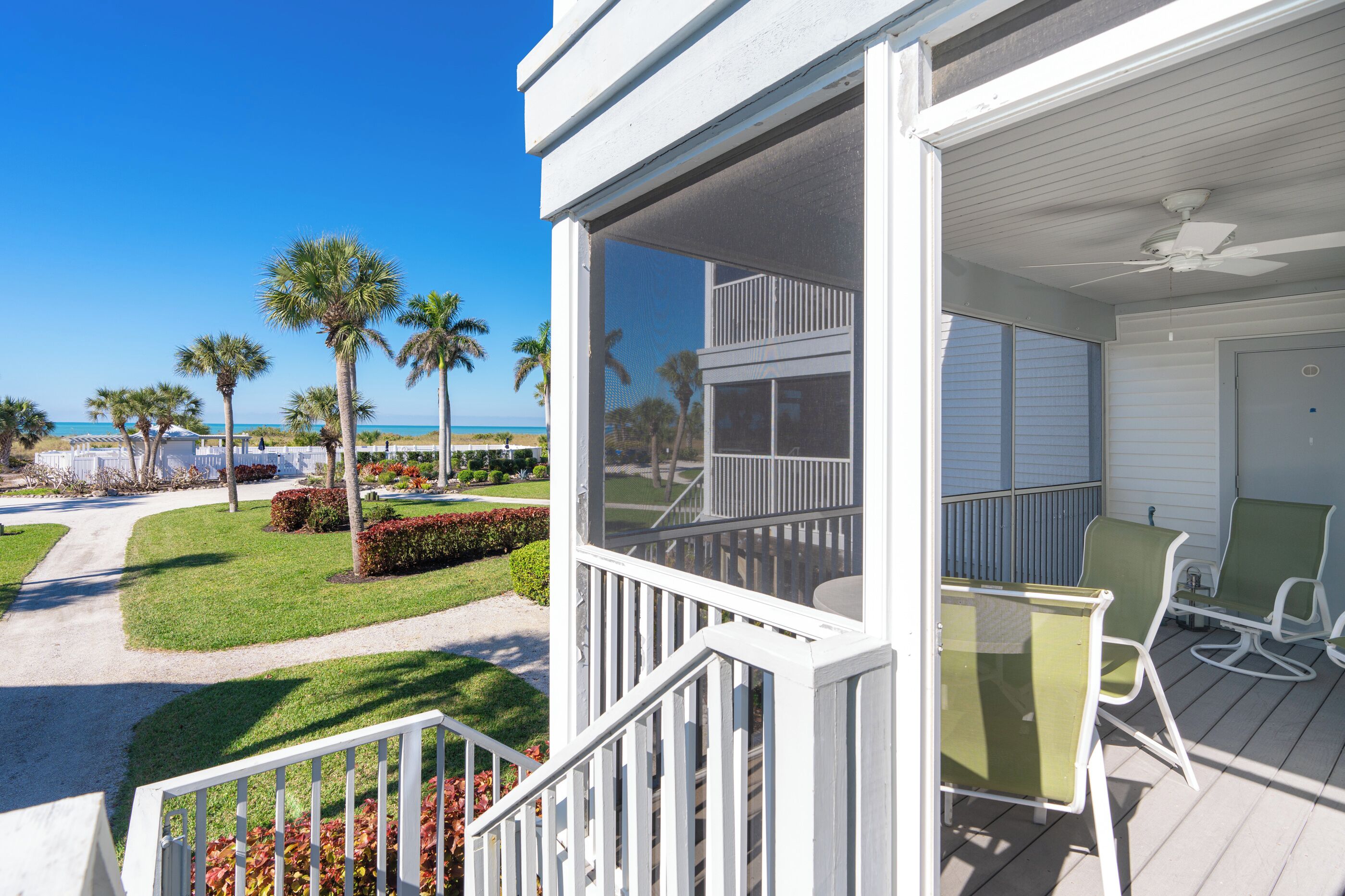 A balcony with a view of the beach, a pool, and a house with a screened porch.