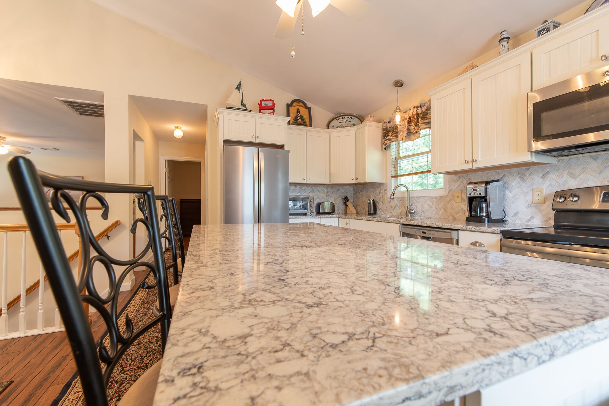 A kitchen with white cabinets, a stainless steel refrigerator, a large marble countertop, and a black chair.