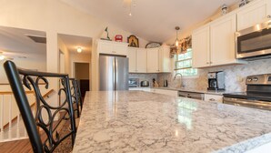 A kitchen with white cabinets, a stainless steel refrigerator, a large marble countertop, and a black chair. - Relax by the sea! 4 bedroom retreat in Bonnet Shores. Central Air sleeps 8A & 2C (Narragansett)