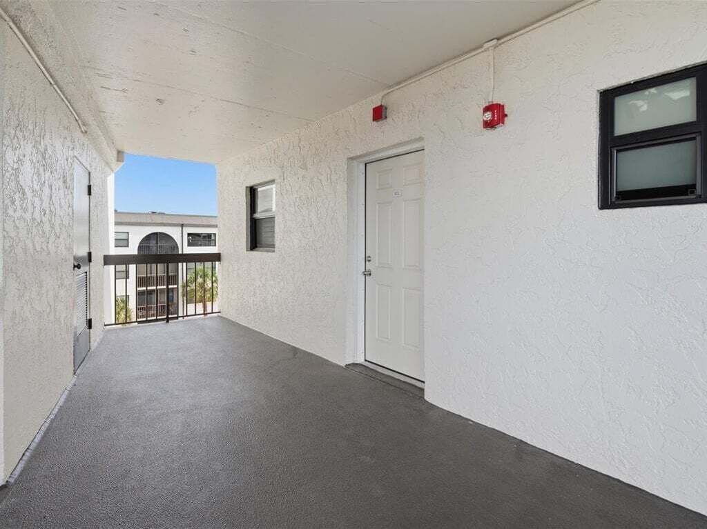 A corridor with a white door, a window, and a red fire alarm.