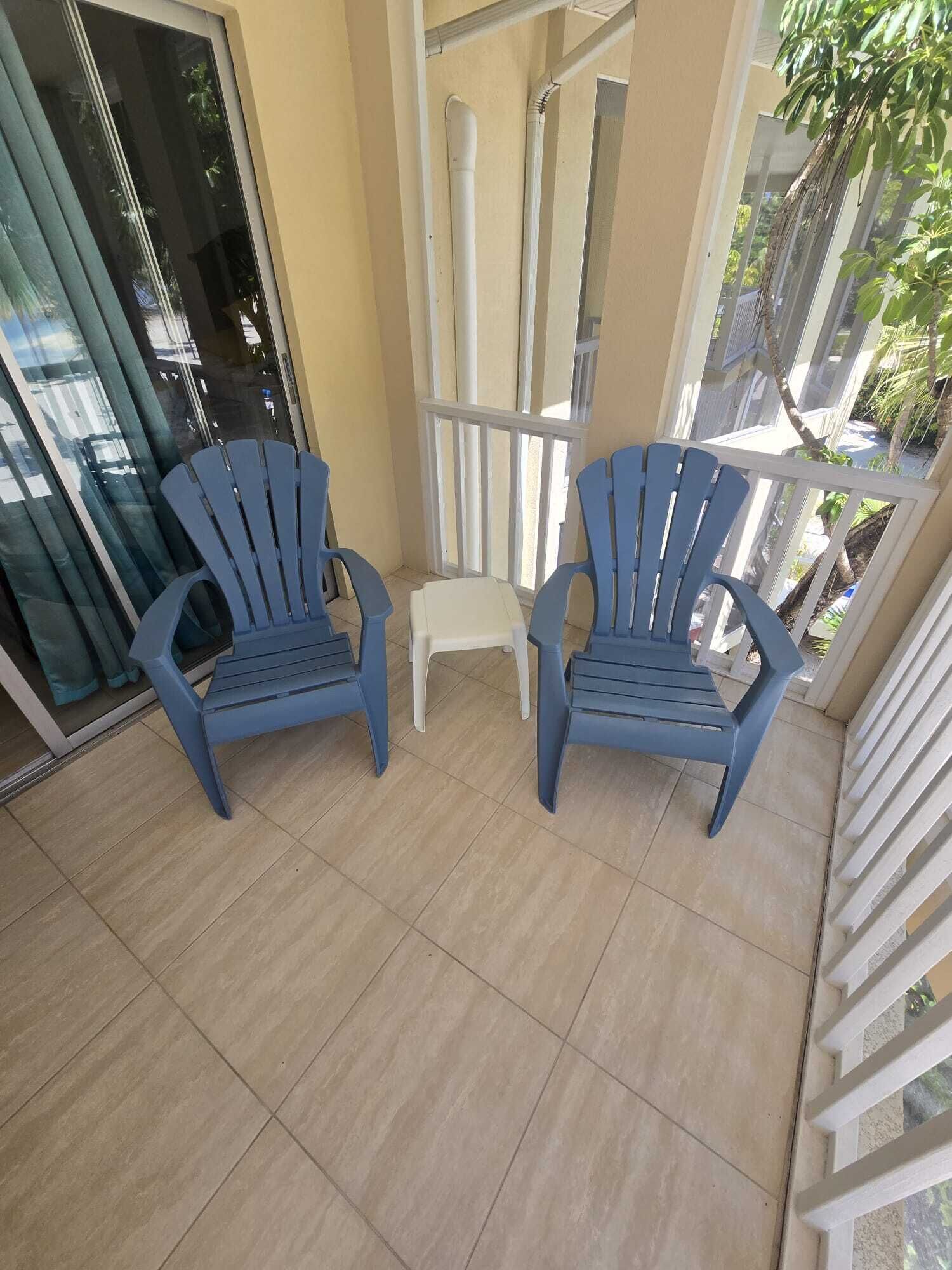 A balcony with two blue chairs, a small white stool, and a glass door.
