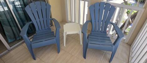 A balcony with two blue chairs, a small white stool, and a glass door.
