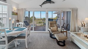 A spacious room with a dining table, chairs, a recliner, and a ceiling fan. - Enjoy a Beautiful Gulf Sunset from the Screened Porch on Resort Villa A3221B (Cape Haze)