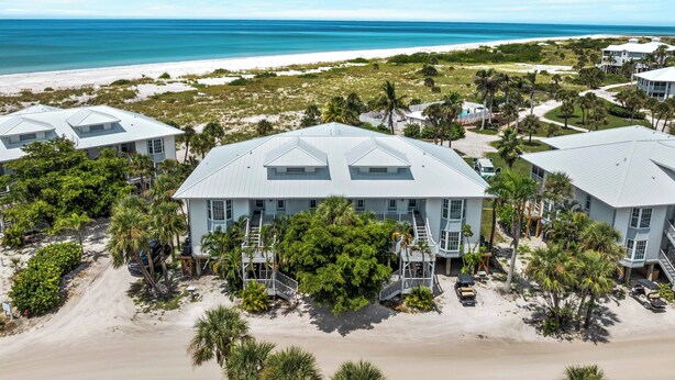 A beachfront property with multiple buildings, including a central structure with a prominent staircase and a smaller building to the right. - Enjoy a Beautiful Gulf Sunset from the Screened Porch on Resort Villa A3221B (Cape Haze)