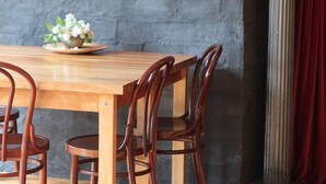 Une table à manger en bois, avec quatre chaises, un vase de fleurs et un tableau encadré sur un mur gris.