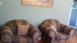 Two plaid armchairs with wooden legs and a cushion, positioned on a wooden floor against a light blue wall with a framed landscape painting above. - Ideal for families and groups (Buchan)