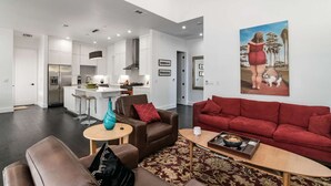 A spacious living area with a red sofa, a brown armchair, and a coffee table. There is a kitchen in the background with white cabinets and a stainless steel refrigerator. - Austin Compound 1 Block off Trendy South Congress, Perfect for Groups Traveling Together! (Austin)