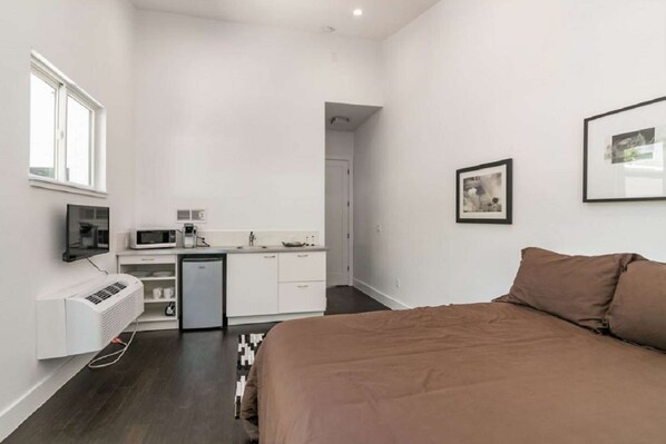 A compact hotel room with a bed, a kitchenette, a small bathroom, and a window. - Austin Compound 1 Block off Trendy South Congress, Perfect for Groups Traveling Together! (Austin)