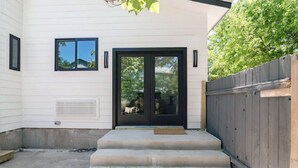 A house with a black front door, two windows, a wooden fence, and a concrete staircase leading to the door. - Austin Compound 1 Block off Trendy South Congress, Perfect for Groups Traveling Together! (Austin)