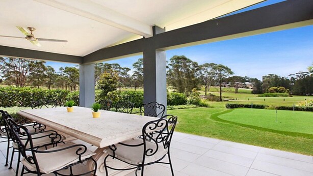 A covered patio with a table and chairs, a ceiling fan, and a view of a well-maintained lawn and trees.