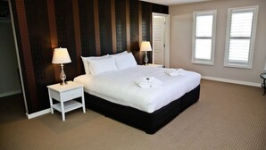 A neatly arranged hotel room with a large bed, two bedside tables with lamps, a door, and two windows.