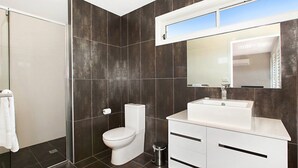 A modern bathroom with dark tiled walls, a white toilet, a white sink, and a mirror above the sink.