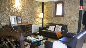 A living room with a stone wall, a black leather sofa, a coffee table, and a lamp. - Ca l'Helena. Enjoy the Penedès, the wine region of Barcelona (Castellet i la Gornal)