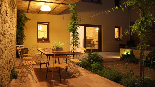 An outdoor patio with a table and chairs, surrounded by plants and a stone wall. - Ca l'Helena. Enjoy the Pened ès, the wine region of Barcelona (Castellet i la Gornal)