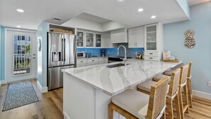 Cozinha moderna com armários brancos, uma ilha grande, eletrodomésticos de aço inoxidável e painel de fundo azul.