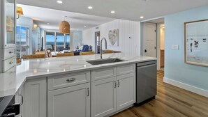 Cozinha moderna com uma ilha grande, armários brancos e vista para a sala de jantar.
