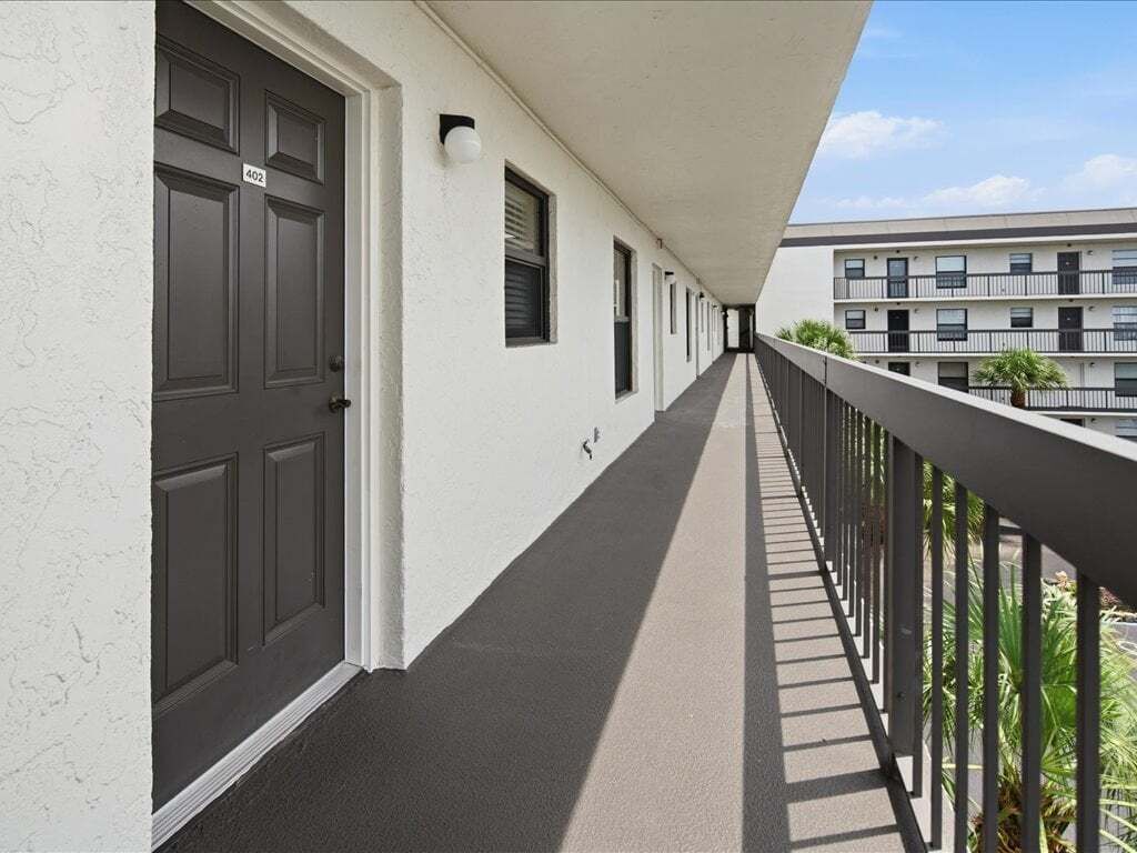 A corridor with doors, a balcony with a railing, and a building in the background.