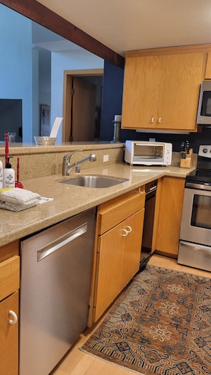 A kitchen with stainless steel appliances, wooden cabinets, a granite countertop, and a patterned rug. - Snowcreek Resort Vacation Rental 838 (Mammoth Lakes)