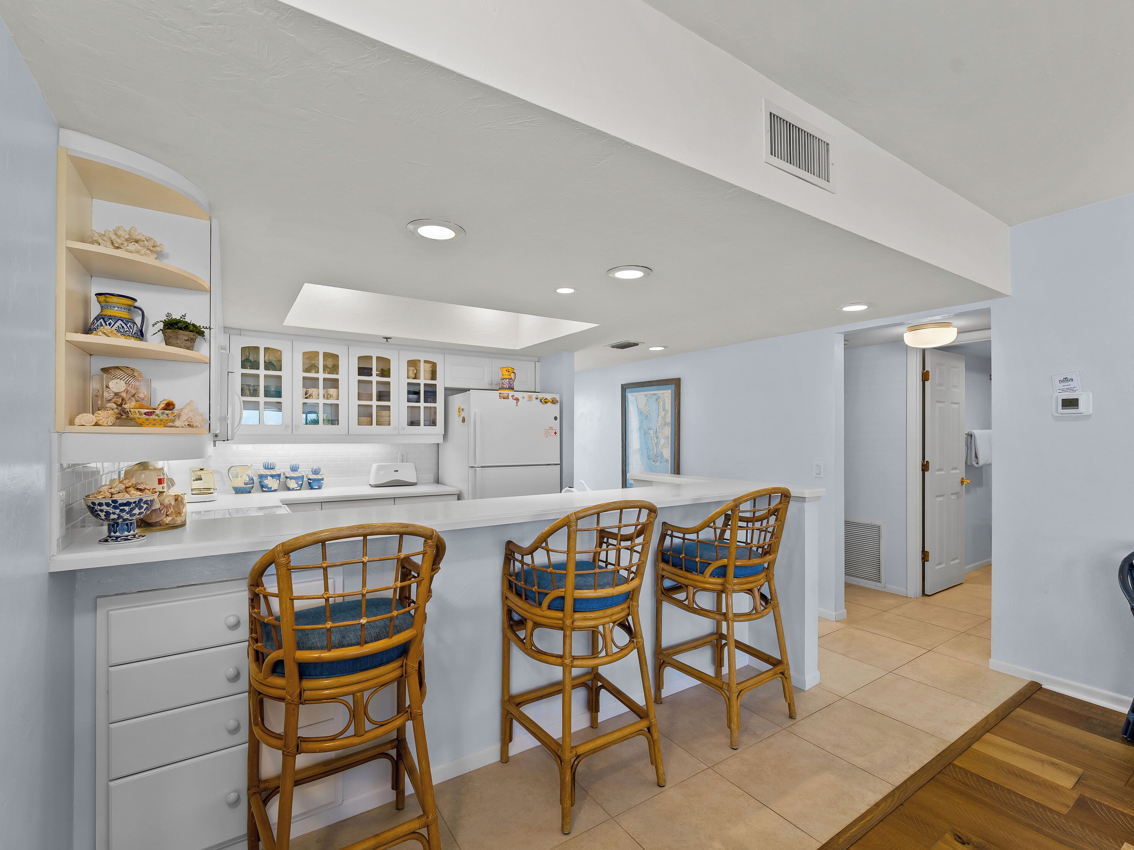 A modern kitchen with white cabinetry, a central island with bar stools, and a refrigerator with magnets.