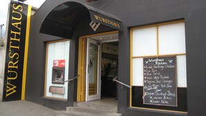 A black building with a sign reading "WURSTHAUS" and a chalkboard menu listing items like "Nichols Free Range Chickens" and "Fresh Whole Rabbits".